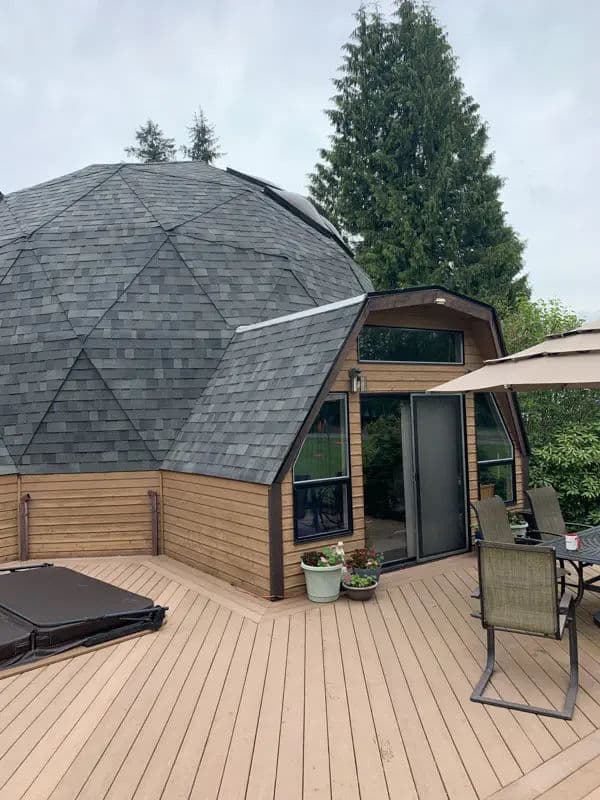 Geodesic dome home with wooden deck, surrounded by greenery and outdoor seating.